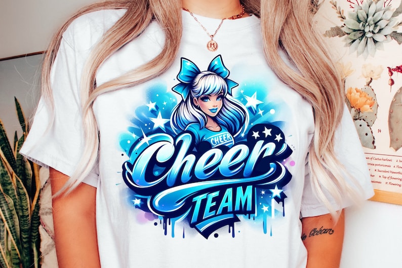 May include: White t-shirt with a blue and white graphic design of a cheerleader with a blue bow in her hair. The graphic says "Cheer Team" in blue and white lettering.