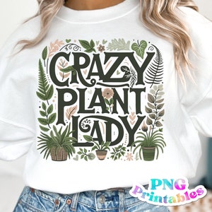 May include: White sweatshirt with a green and brown graphic design that says "Crazy Plant Lady". The design features a variety of plants and flowers.