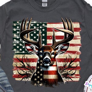 May include: Dark gray t-shirt featuring a deer head design with antlers, superimposed over a distressed American flag. The deer's face is colored with the flag's stars and stripes. The shirt is a casual wear item.