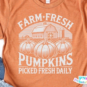 May include: Orange t-shirt with a white graphic design of a farm scene with pumpkins and the text "Farm Fresh Pumpkins Picked Fresh Daily".