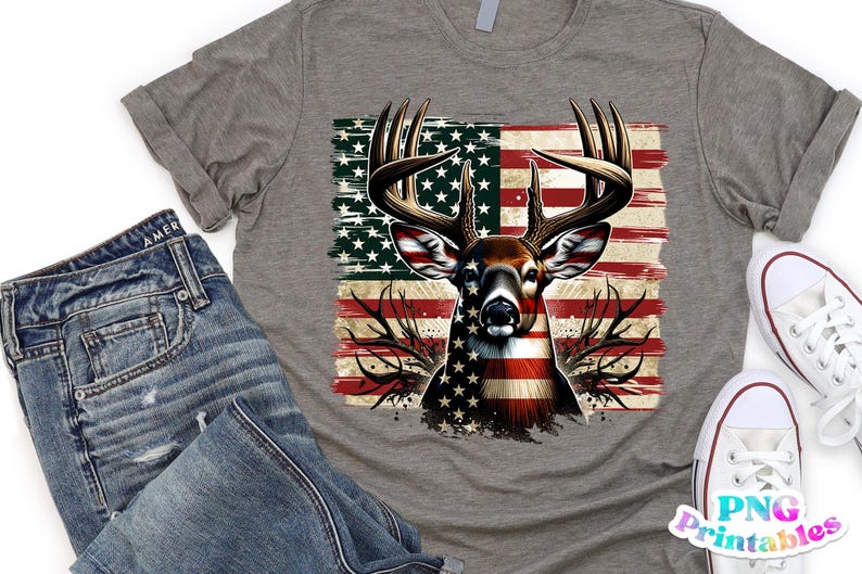May include: A heather gray t-shirt featuring a deer design with an American flag motif. The deer's body is colored with the stars and stripes. The shirt is paired with blue jeans and white sneakers.