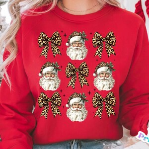 May include: Red sweatshirt with a repeating pattern of Santa Claus faces and leopard print bows.