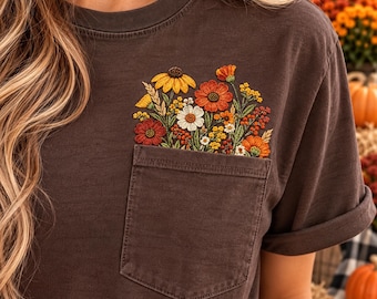 May include: A dark brown short-sleeve t-shirt featuring a chest pocket with an embroidered floral arrangement. The embroidery displays a variety of flowers in shades of orange, yellow, red, and white, with green stems and leaves emerging from the pocket.