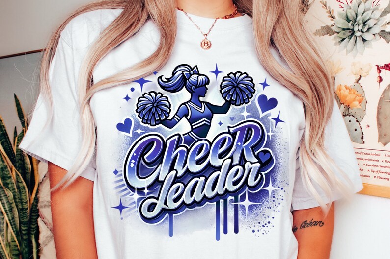 May include: White t-shirt with a blue and purple graphic design of a cheerleader holding pom-poms. The text "Cheerleader" is written in a stylized font.