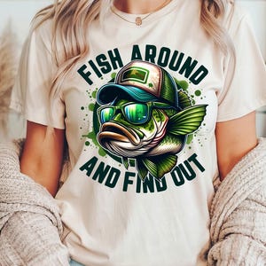 May include: A white t-shirt with a green and black cartoon fish wearing sunglasses and a baseball cap. The text "Fish Around And Find Out" is printed on the shirt.