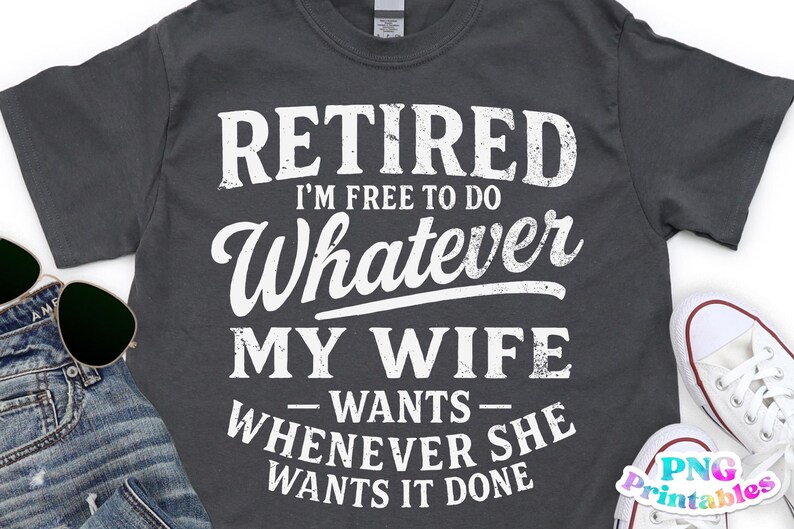 May include: Dark grey t-shirt with the text "RETIRED I'M FREE TO DO WHATEVER MY WIFE WANTS WHENEVER SHE WANTS IT DONE" in white. The shirt is styled with sunglasses, jeans, and white trainers.