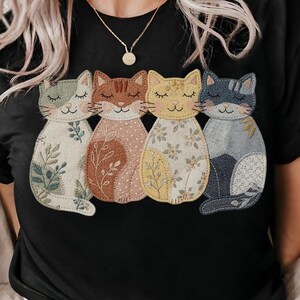 Pu&ograve; includere: T-shirt nero con un disegno di quattro figure di gatti stilizzate. Ogni gatto ha un colore e un motivo unici, tra cui motivi floreali e a foglie. I gatti sono in tonalit&agrave; di verde, marrone, giallo e blu, con gli occhi chiusi e i baffi.