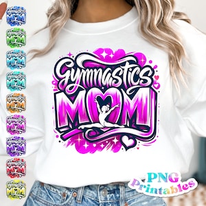 Op de afbeelding: Wit sweatshirt met een roze en paarse grafische print met de tekst "Gymnastics Mom" en een silhouet van een turnster in een hartvorm. Het ontwerp is omringd door sterren en harten.