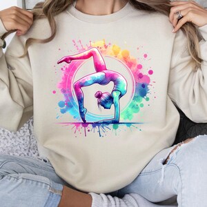 May include: A cream colored sweatshirt with a colorful watercolor design of a woman doing a backbend yoga pose.