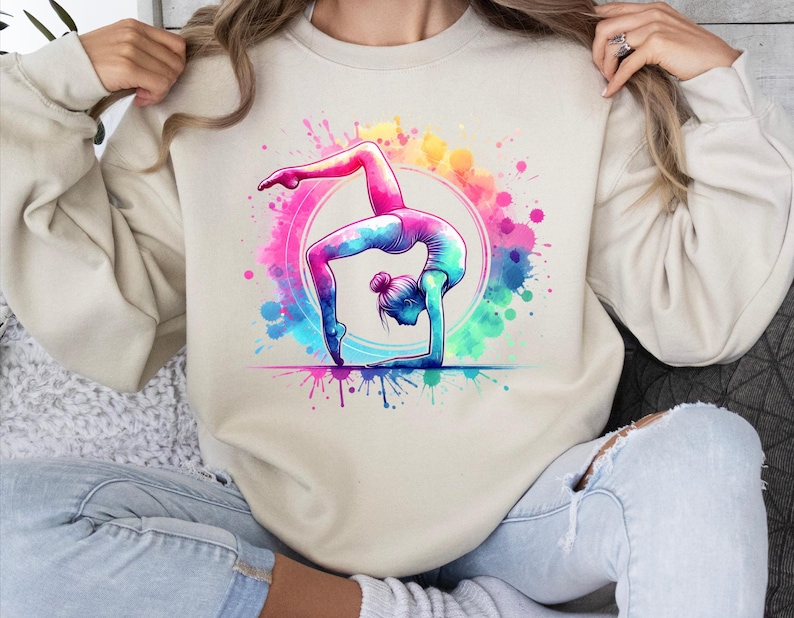 May include: A cream colored sweatshirt with a colorful watercolor design of a woman doing a backbend yoga pose.