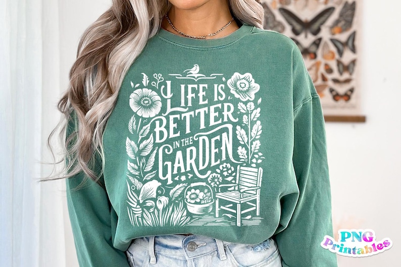 May include: A green sweatshirt with a white graphic design that says "Life is better in the garden". The graphic includes flowers, leaves, a bird, and a chair.