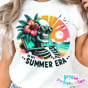 May include: A white t-shirt with a graphic of a skeleton wearing sunglasses and a flower behind its head. The skeleton is sitting on a beach with a sunset in the background. The text "In My Summer Era." is printed below the graphic.