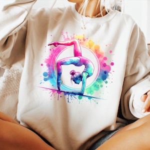 May include: A white sweatshirt with a colorful watercolor design of a person doing a handstand. The design features splashes of pink, blue, green, and yellow.