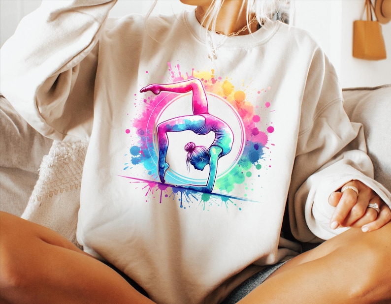 May include: A white sweatshirt with a colorful watercolor design of a person doing a handstand. The design features splashes of pink, blue, green, and yellow.
