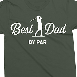 K&ouml;nnte beinhalten: Dunkelgr&uuml;nes T-Shirt mit dem Text "Best Dad" in Schreibschrift und "BY PAR" in einer serifenlosen Schriftart. Eine wei&szlig;e Silhouette eines Golfspielers beim Schwingen des Schl&auml;gers befindet sich zwischen den W&ouml;rtern. Das Shirt ist aus weichem Material.