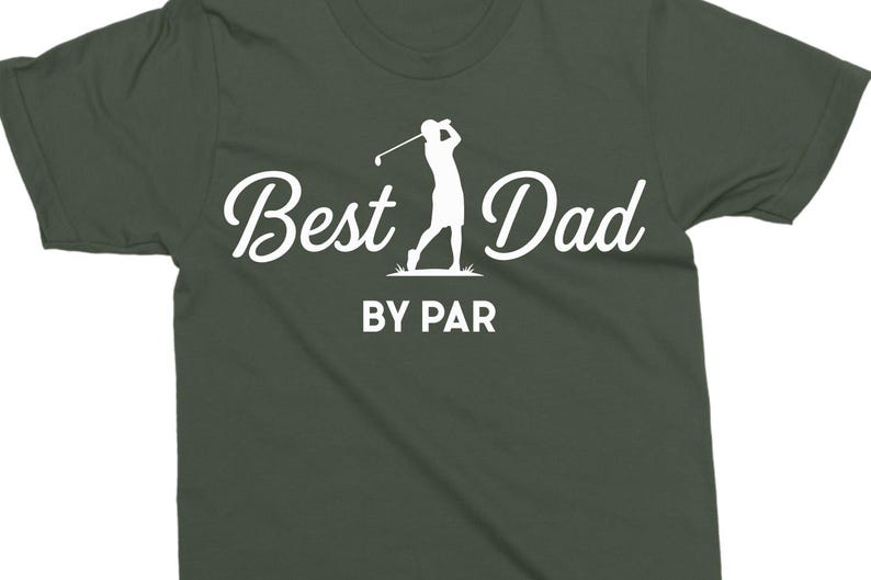 K&ouml;nnte beinhalten: Dunkelgr&uuml;nes T-Shirt mit dem Text "Best Dad" in Schreibschrift und "BY PAR" in einer serifenlosen Schriftart. Eine wei&szlig;e Silhouette eines Golfspielers beim Schwingen des Schl&auml;gers befindet sich zwischen den W&ouml;rtern. Das Shirt ist aus weichem Material.