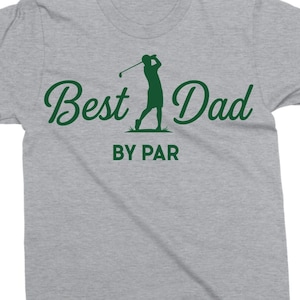 K&ouml;nnte beinhalten: Hellgraues T-Shirt mit dem gr&uuml;nen Schriftzug "Best Dad" und einer gr&uuml;nen Silhouette eines Golfspielers. Der Text "BY PAR" befindet sich unter dem Haupttext.