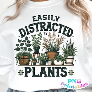 Könnte beinhalten: Weißes Sweatshirt mit einem grünen und braunen Grafikdesign, auf dem "Leicht abgelenkt von Pflanzen" steht.