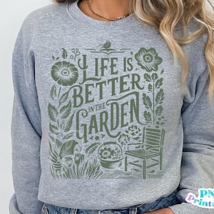 May include: Gray sweatshirt with a green graphic design that says "Life is better in the garden". The graphic includes a bird, flowers, and a chair.