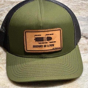 Puede incluir: Un gorro de camionero verde y negro con un parche de cuero marrón que dice "Anatomy of a Pew" y "NC Hat Co."