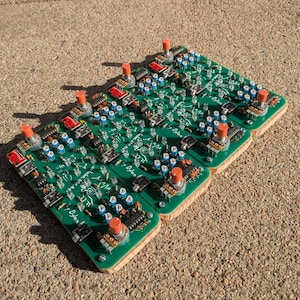 Puede incluir: Cuatro placas de circuito verde con botones rojos y componentes azules están montadas en bases de madera. Las placas están etiquetadas "Dylan F."