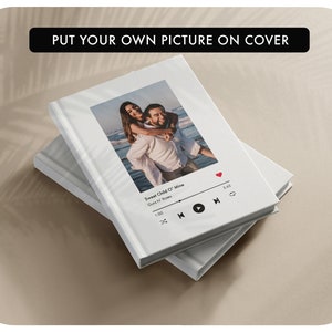 May include: White photo album with a white cover and a photo of a couple on the beach. The album has a music player interface with the song "Sweet Child O' Mine" by Guns N' Roses playing.