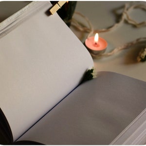 May include: An open blank journal with white pages, a lit candle, and white string on a white surface.