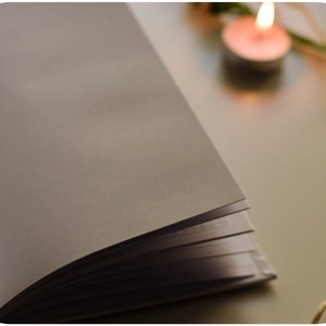 May include: A white notebook with a blank page open, lying on a white surface. A lit candle and a piece of twine are in the background.