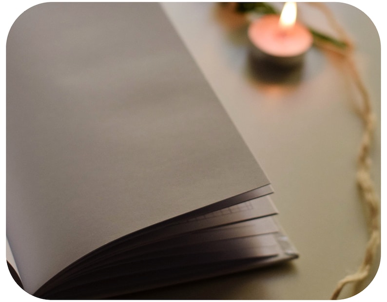 May include: A white notebook with a blank page open, lying on a white surface. A lit candle and a piece of twine are in the background.