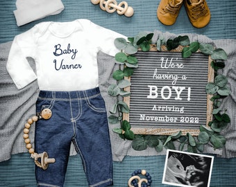 May include: A flat lay featuring baby clothes and accessories. Includes a white onesie with "Baby Varner" in navy script, denim pants, a pacifier, a letter board announcing "We're having a BOY!" and baby shoes. An ultrasound image is also present.