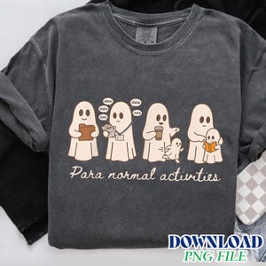 Peut inclure: Un t-shirt à col rond gris anthracite avec un motif représentant quatre fantômes effectuant des tâches quotidiennes. Le texte "Para normal activities" est imprimé sous les fantômes. Un fantôme tient un dossier, un autre porte un badge et des papiers, un troisième tient un café, et le dernier lit un livre à un plus petit fantôme.
