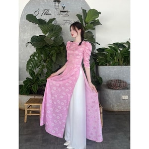 May include: A pink and white dress with a floral pattern. The dress has a high neck and long sleeves. The dress is split at the front and has a white underskirt.