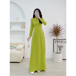 Könnte beinhalten: Ein langes, lindgrünes Kleid mit einem Mandarinkragen und langen Ärmeln. Das Kleid hat einen seitlichen Schlitz und ist aus glattem Stoff gefertigt.