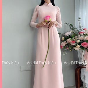 Könnte beinhalten: Ein rosafarbenes, langärmeliges Kleid mit einem Mandarinkragen und einem Lotusblumenmuster. Das Kleid wird von einer Frau getragen, die eine rosafarbene Lotusblume hält. Der Text "MÃ: CF01 Hồng Phớt" befindet sich am unteren Rand des Bildes.