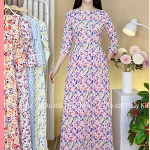 May include: A long, white dress with a floral print in shades of pink, blue, and green. The dress has a round neckline and three-quarter sleeves. The dress is shown on a model with a white background.