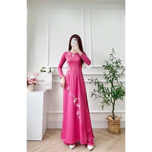 Puede incluir: Un vestido largo de color rosa con un diseño floral. El vestido tiene mangas largas y un escote redondo.