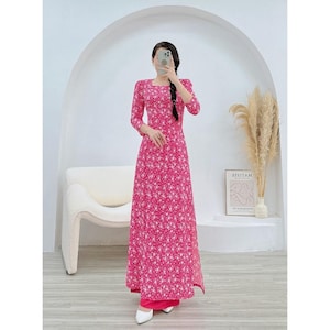 Puede incluir: Un vestido rosa de manga larga con estampado floral blanco. El vestido tiene un escote cuadrado y una abertura lateral. La modelo lleva el vestido con un pantalón rosa.