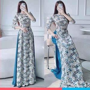 Puede incluir: Un vestido maxi blanco con forro azul turquesa y estampado de hojas. El vestido tiene un escote alto y mangas tres cuartos.