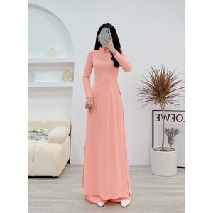 May include: A long, peach-colored dress with a mandarin collar and long sleeves. The dress has a fitted bodice and a flowing skirt.