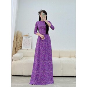 Könnte beinhalten: Ein langes, lila Kleid mit floralem Muster. Das Kleid hat einen hohen Ausschnitt und Dreiviertelärmel. Das Kleid ist bodenlang und scheint aus einem leichten Stoff zu sein.