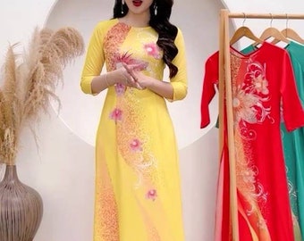 May include: A yellow dress with a floral pattern and a white background. The dress has a round neckline and three-quarter sleeves. The dress is on a mannequin and the text "Mã: K150" is at the bottom of the image.