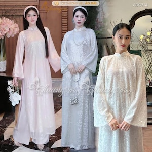 May include: Three women modelling sequined áo dài dresses in white and pink. The dresses feature long sleeves and a high collar. The text "Chuang May" is visible on the dresses. The top right corner of the image has the text "ADC714".