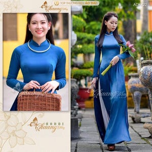 May include: Two women wearing long-sleeved, blue áo dài dresses. The dresses have a mandarin collar and a split skirt. One woman holds a woven basket, the other holds flowers. The dresses are a solid blue color.
