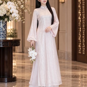 May include: A pale pink long-sleeved tunic with a high collar and all-over sequin embellishments, paired with matching wide-leg trousers. The tunic features side slits and flared sleeves, creating a flowing silhouette with a shimmering finish.