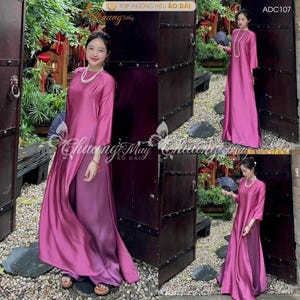 May include: A magenta Áo dài dress with a high collar and long sleeves. The dress has a split front, showing a lighter magenta underlayer. The model wears a pearl necklace and holds a fan. The text "Chuang May Ao Dai" is visible.