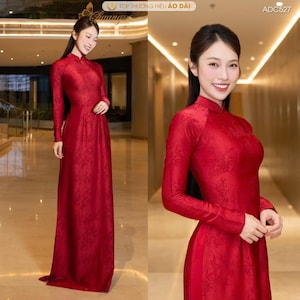 May include: A long, red dress with long sleeves and a high collar. The dress has a subtle floral pattern and is worn by a person. The image also includes the text "TOP THƯƠNG HIỆU ÁO DÀI" and "ADC527".