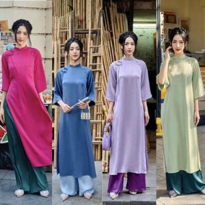 以下が含まれることがあります： 4人の女性が、ピンク、ブルー、パープル、グリーンの異なる色の長い伝統的なベトナムのドレスを着ています。各ドレスは、マンダリンカラーとフロントにボタンが付いています。女性たちは、ドレスの色よりも濃い色のパンツを合わせています。