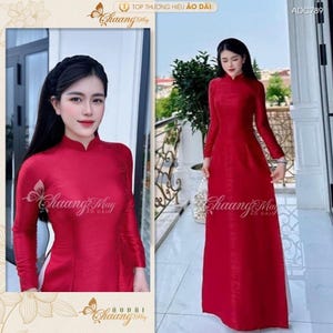 May include: A vibrant red Áo dài dress with long sleeves and a mandarin collar. The dress features a subtle sheen and a flowing silhouette. The image includes the text "Chaang May" and "TOP THƯƠNG HIỆU ÁO DÀI".