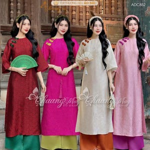 May include: Four women wearing traditional Vietnamese áo dài dresses in shades of red, fuchsia, cream, and pink. Each dress features decorative accents and is paired with contrasting pants. The image includes text in Vietnamese.