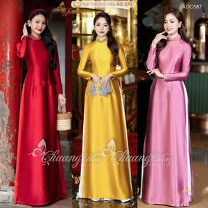 May include: Three women modelling long, flowing dresses in red, yellow, and pink. Each dress has long sleeves and a mandarin collar. The dresses feature a butterfly design and text. The dresses are made of a shiny fabric.